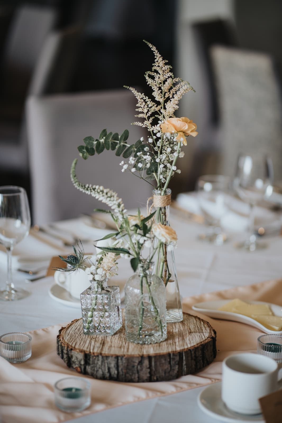 Bud vases of peach roses, astilbe and eucalyptus on a rustic wood round at a set reception table