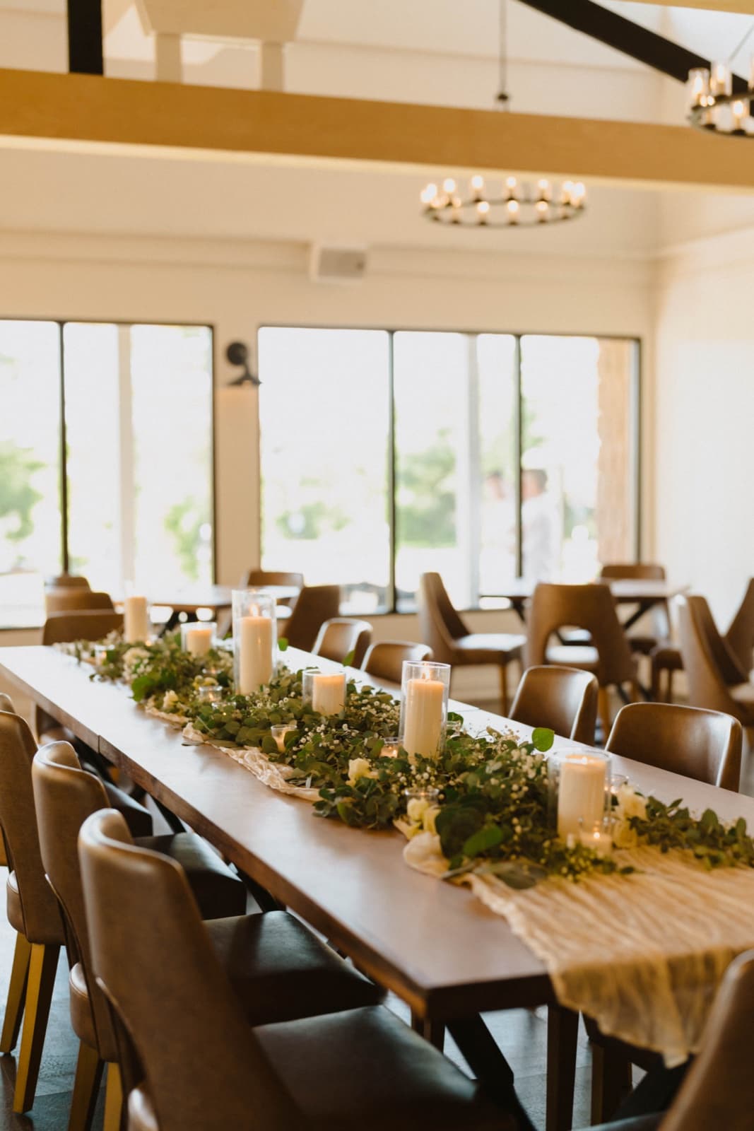 A greenery garland with pillar candles running down a long head table in a bright hall
