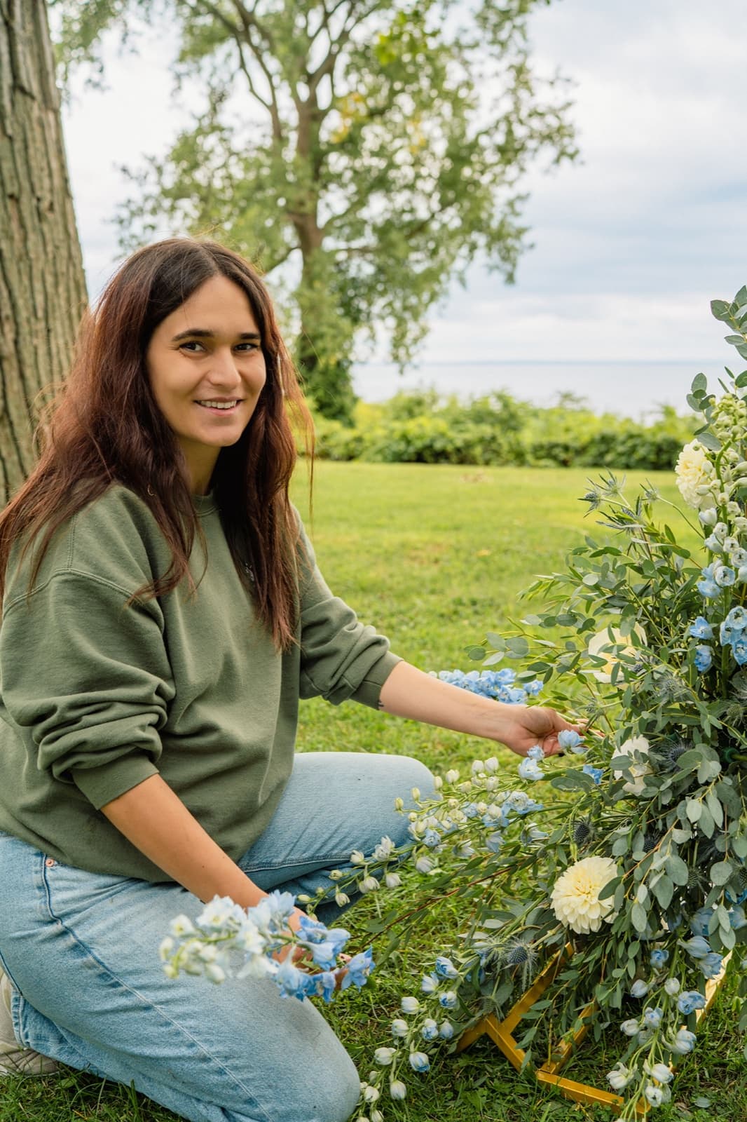 Antonia Waller, lead designer at sunnmoon, styling a blue and white arch arrangement by the lake