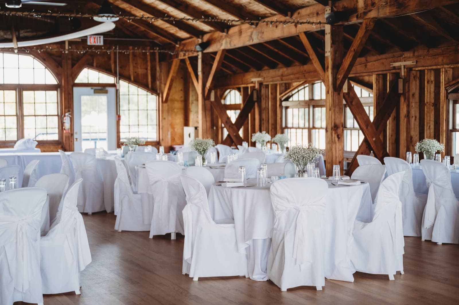 Round tables in white covers with baby's breath centerpieces in a timber-frame hall