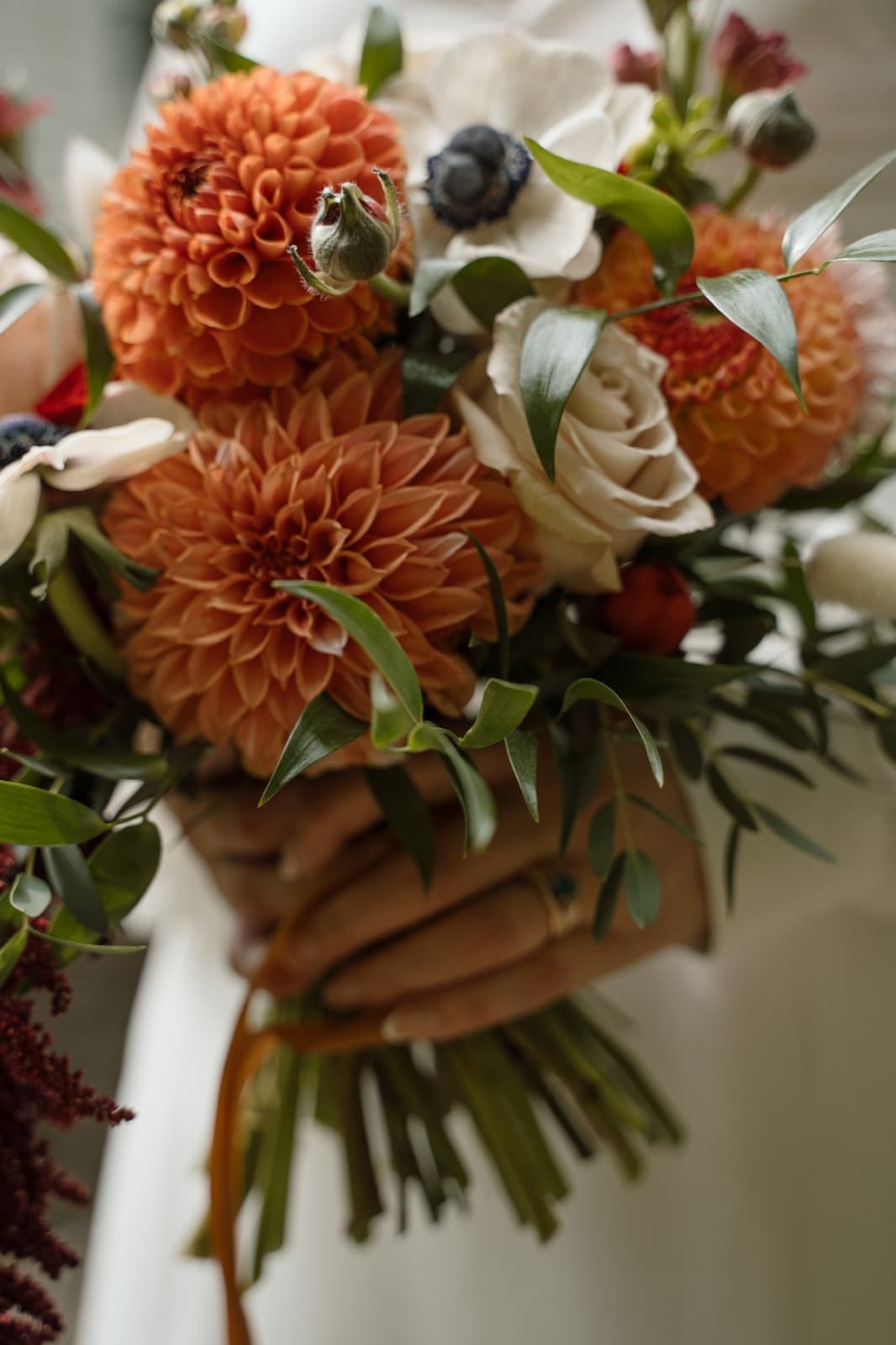 Close-up of a bridal bouquet of orange dahlias, white anemones and blush roses