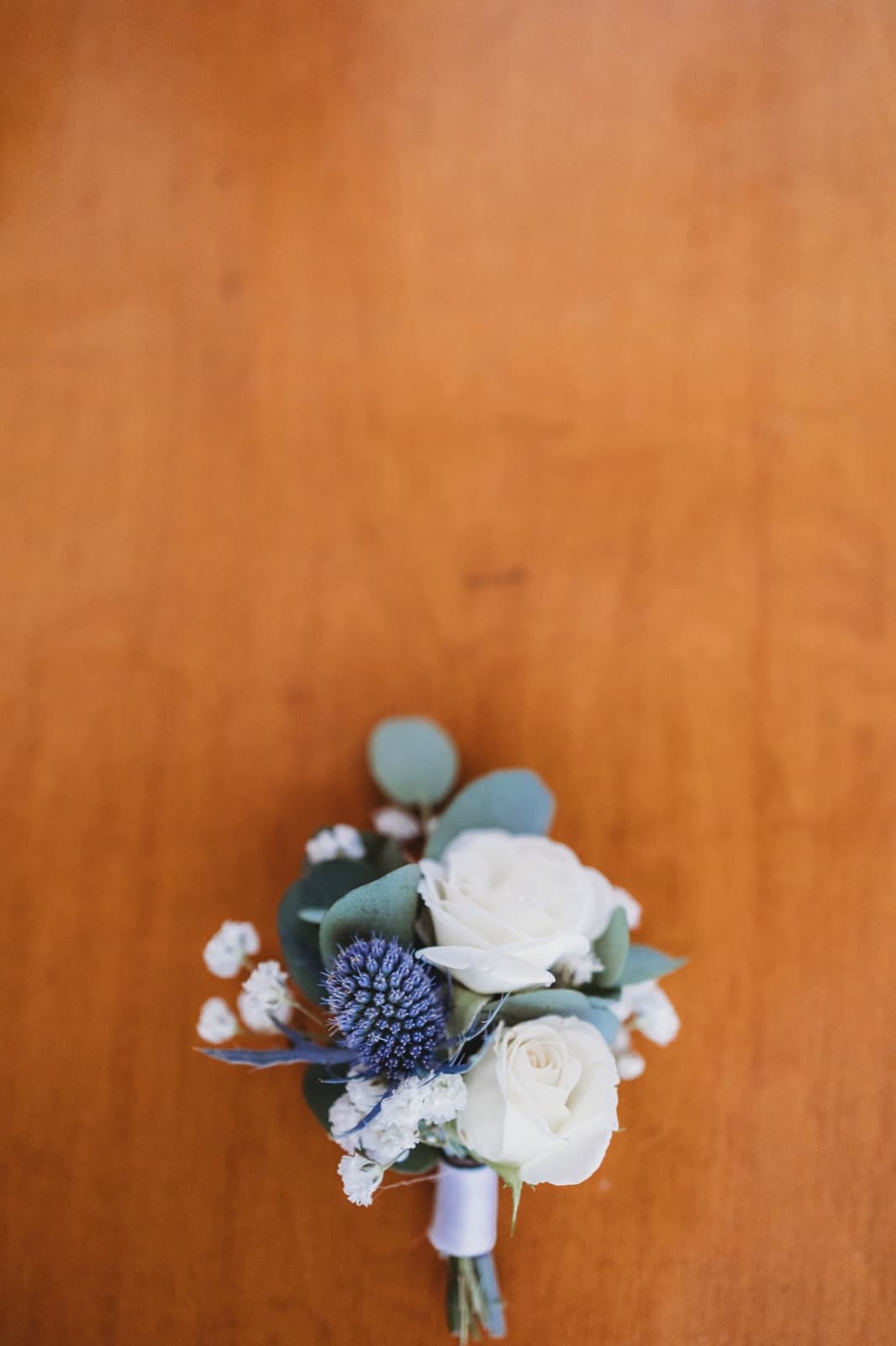 A boutonniere of white spray roses, blue sea holly and eucalyptus on a wooden table