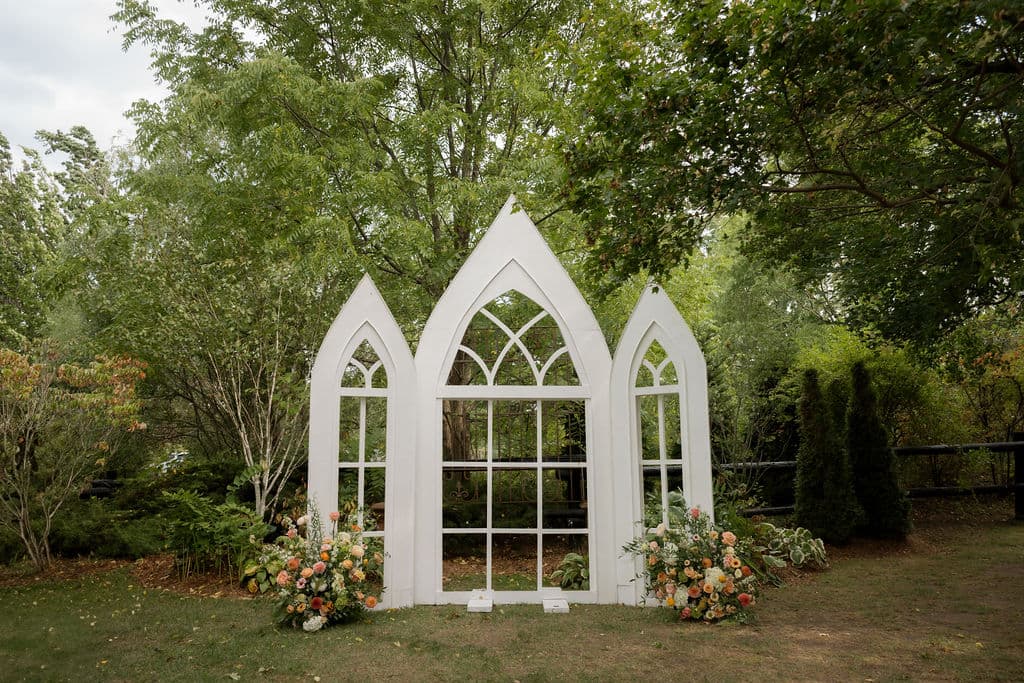 A ceremony backdrop of three arched chapel window frames flanked by peach and white arrangements