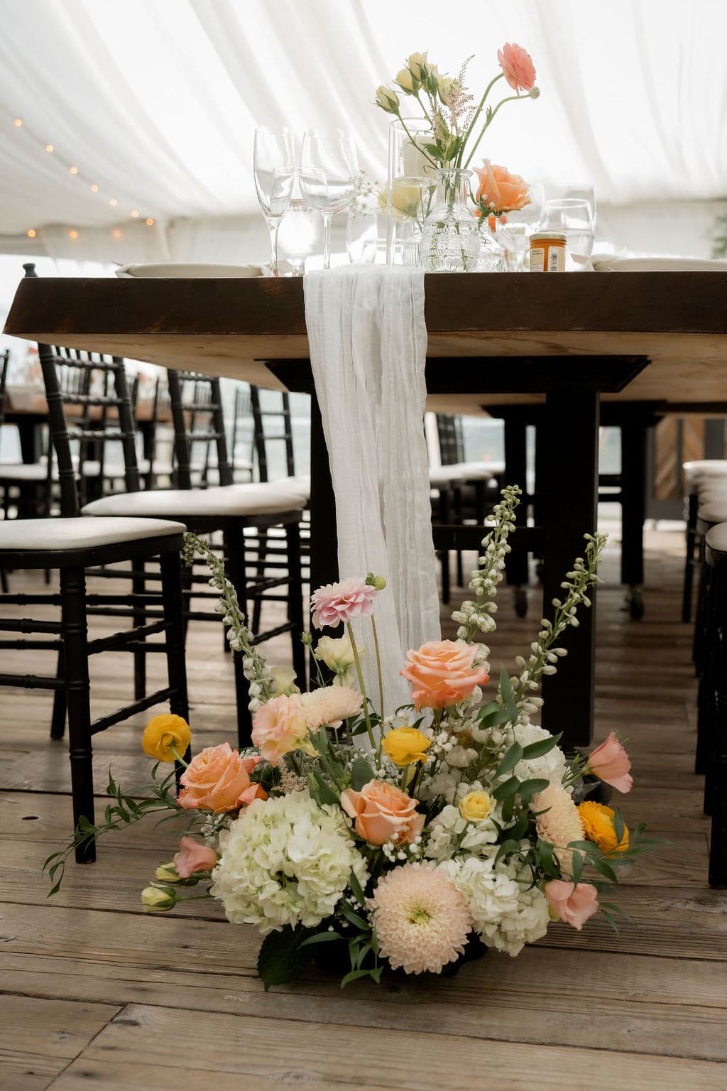 An arrangement of peach roses, hydrangea and dahlias at the base of a head table draped with a gauze runner