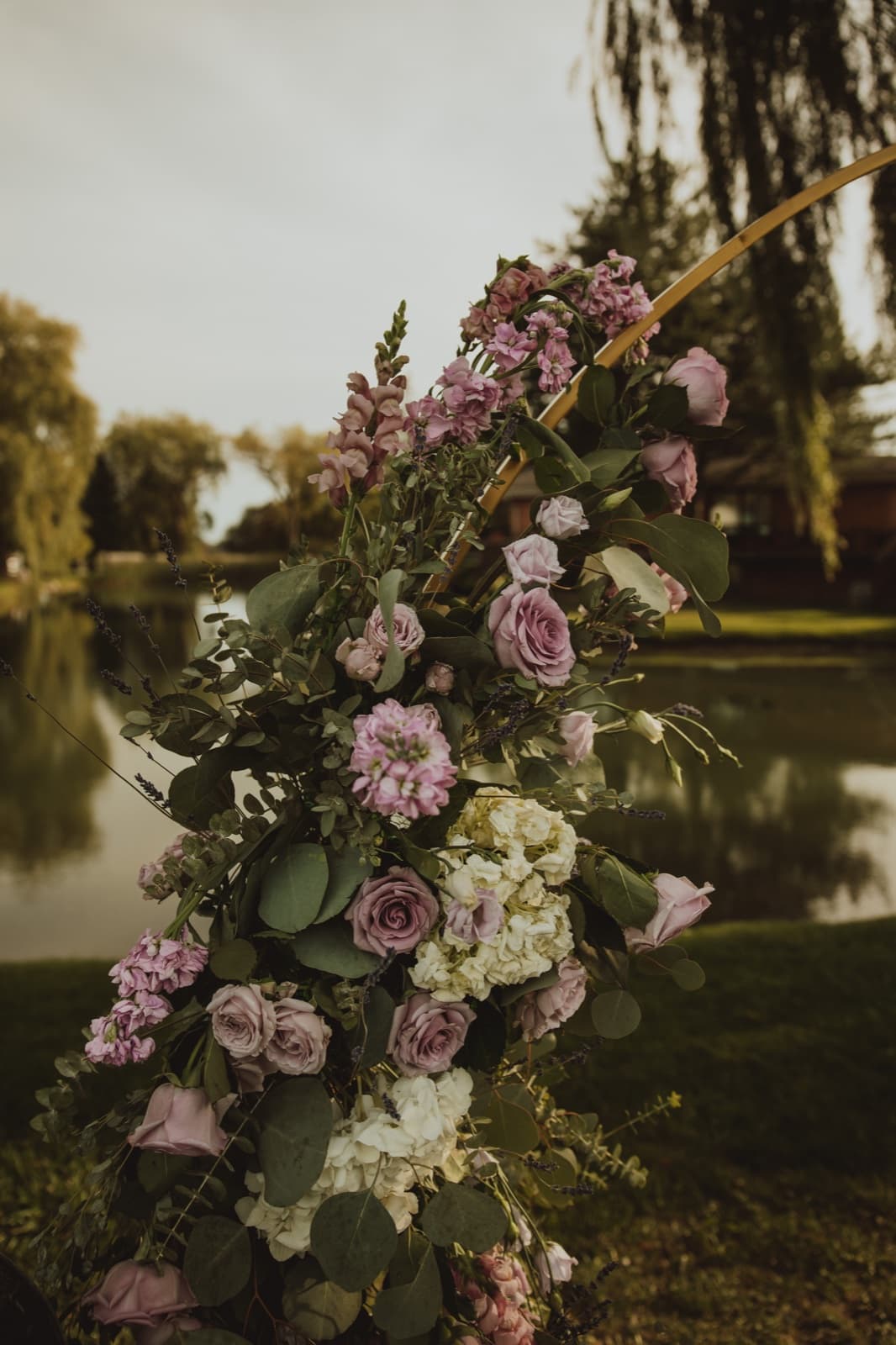 Mauve roses, snapdragons and hydrangea climbing a gold hoop arch at the water's edge