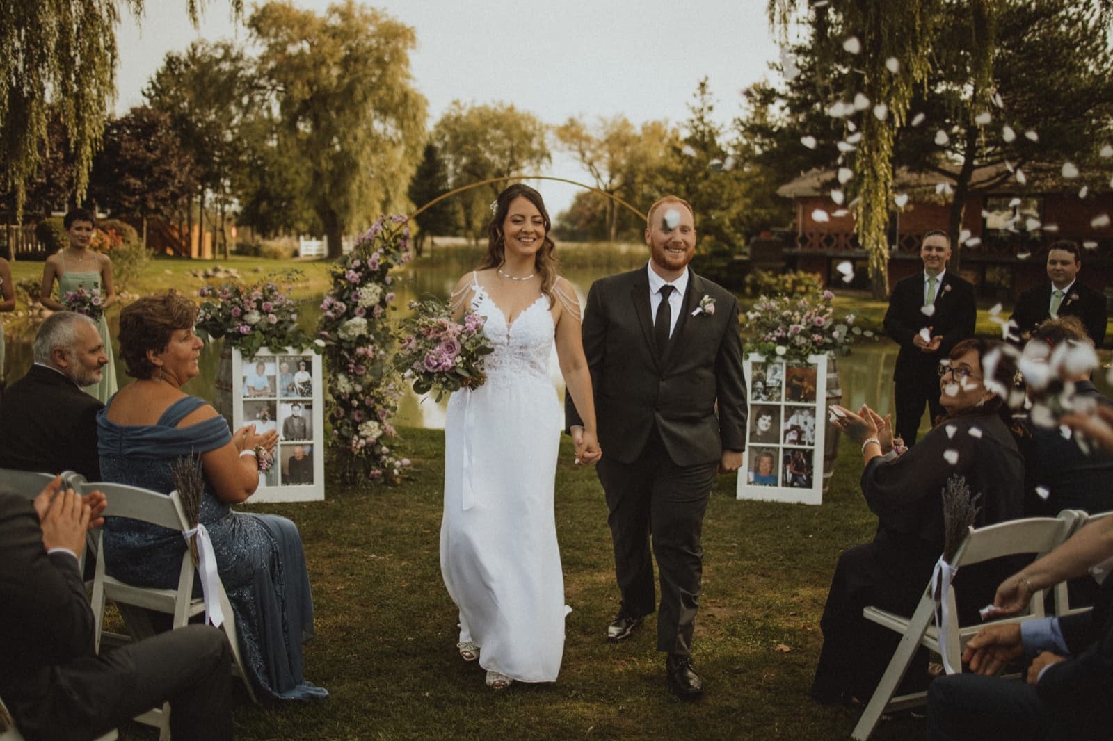 Newlyweds walking back up the aisle through tossed petals, the bride carrying a mauve rose bouquet