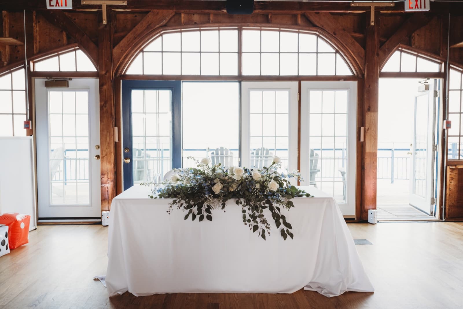 A sweetheart table with a garland of greenery and white roses set before glass doors